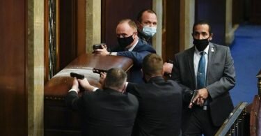 Sicherheitsleute des Kapitols stehen mit gezogenen Waffen hinter einer verbarrikadierten Tür. Foto: Andrew Harnik/AP/dpa