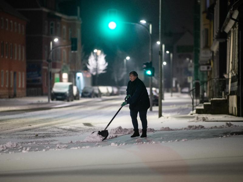 Eine Frau schippt am frühen Morgen Schnee auf einem Bürgersteig in Gevelsberg. Foto: Jonas Güttler/dpa
