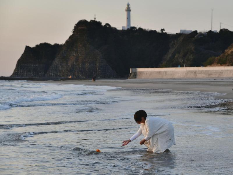 Eine Frau legt in Gedenken an die Opfer der Fukushima-Katastrophe Blumen an einem Strand in der nordostjapanischen Stadt Iwaki ab. Foto: ---/kyodo/dpa