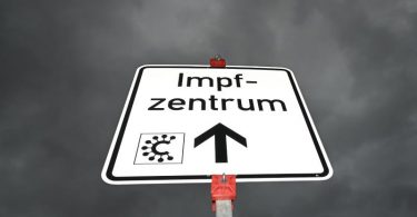 Ein Hinweisschild mit der Aufschrift «Impfzentrum» und einem Covid-Logo ist nahe des Impfzentrums Heuchelheim zu sehen. Foto: Arne Dedert/dpa