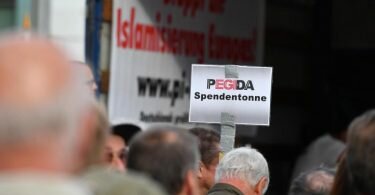 Auf einer Kundgebung von Pegida halten Anhänger ein Schild mit dem Schriftzug «Pegida Spendentonne» in die Höhe. Foto: Zentralbild/dpa-Zentralbild/dpa