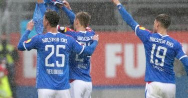 Die Kieler Spieler Phil Neumann (l-r), Hauke Wahl und Simon Lorenz halten nach dem Treffer zum 1:1 ein Trikot des verletzten Mannschaftskameraden Ahmet Arslan hoch. Foto: Frank Molter/dpa