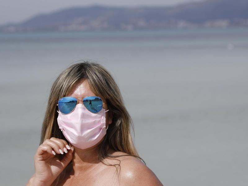 Maske am Strand: Auch 2021 steht der Sommerurlaub - wie hier auf Mallorca - ganz im Zeichen der Pandemie. Foto: Clara Margais/dpa