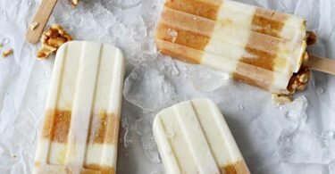 In Stieleis-Formen wird cremige Joghurtmasse abwechselnd mit fruchtiger Nektarinenmasse geschichtet. Das Topping im unteren Teil besteht aus Krümeln eines Erdnussriegels. Foto: Mareike Pucka/biskuitwerkstatt.de/dpa-tmn