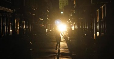 Eine Frau geht im Scheinwerferlicht eines patrouillierenden Polizeiwagens über die Bourbon Street in New Orleans. Foto: Eric Gay/AP/dpa