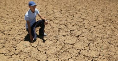 Ein Landwirt kniet auf dem Boden eines ausgetrockneten Wasserlochs in Südafrika. Foto: Denis Farrell/AP/dpa