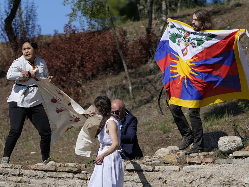 Ein Polizist versucht Demonstranten, die eine tibetische Fahne und ein Transparent mit der Aufschrift «Keine völkermörderischen Spiele» zeigen, aufzuhalten. Foto: Thanassis Stavrakis/AP/dpa