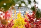Rot-gelb-grün herbstlich verfärbte Blätter sind an Bäumen vor der Reichstagskuppel zu sehen. Foto: Britta Pedersen/dpa-Zentralbild/dpa