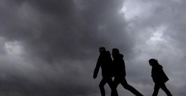 Strand-Spaziergänger unter dunklen Wolken. Foto: Sina Schuldt/dpa