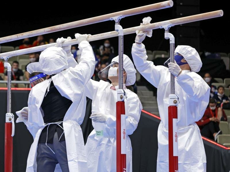 Mitglieder des Organisationsteams desinfizieren in Schutzanzügen und mit Mund-Nasen-Schutz die Geräte. Foto: -/kyodo/dpa/Archivbild