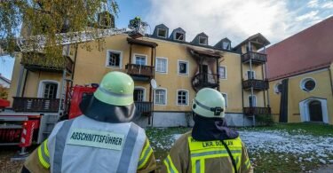 Feuerwehrmänner stehen vor einem ausgebrannten Mehrfamilienhaus. Foto: Armin Weigel/dpa