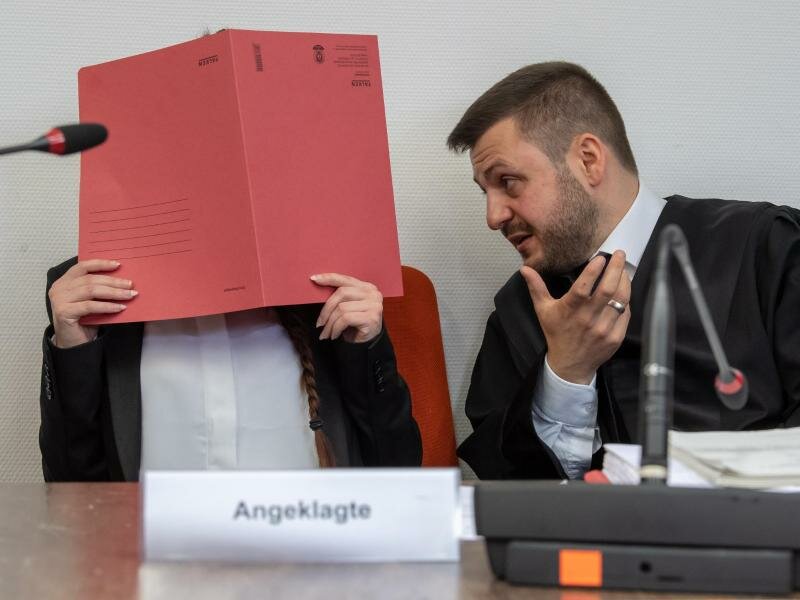 Die Angeklagte Jennifer W. im Gerichtssaal mit einem roten Aktendeckel vor ihrem Gesicht. Foto: Peter Kneffel/dpa