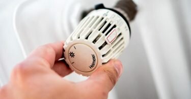 Ein Mann dreht am Thermostat einer Heizung. Foto: Hauke-Christian Dittrich/dpa