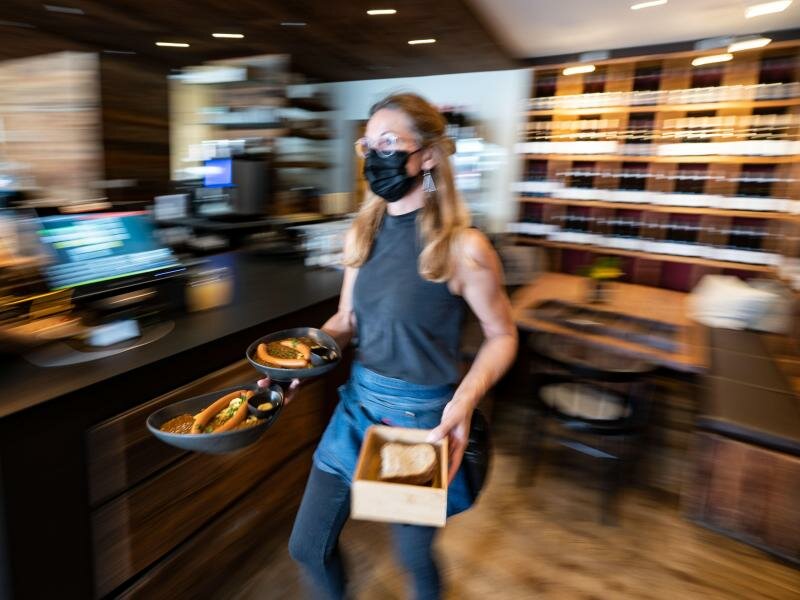 Eine Kellnerin trägt in einem Restaurant Essensteller. (Archivbild). Foto: Marijan Murat/dpa