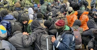 Migranten sitzen zusammen vor der Grenze in Belarus am gesperrten Übergang zu Polen. Foto: Ulf Mauder/dpa