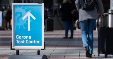 Ein Schild weist auf ein Corona-Testcenter am Flughafen München hin. (Symbolbild). Foto: Sven Hoppe/dpa