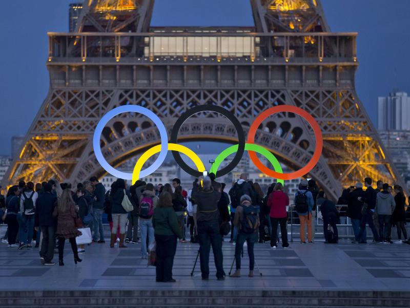 Die Olympischen Ringe leuchten am Fuße des Eiffelturms in Paris. Foto: Michel Euler/AP/dpa