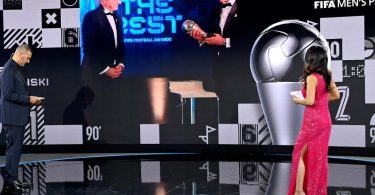 Dem FCB-Stürmer Robert Lewandowski (r. auf Bildschirm) wird 2020 die Weltfußballer-Trophäe überreicht. Foto: Valeriano Di Domenico/POOL FIFA/Getty/dpa