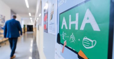 An der Wand eines Flurs in einem Gymnasium ist ein Hinweis auf die AHA-Regeln angebracht. Das Infektionsrisiko ist durch Omikron gerade extrem hoch. Foto: Nicolas Armer/dpa