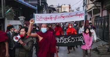 Junge Aktivisten und buddhistische Mönche nehmen an einer Protestkundgebung gegen die Militärregierung teil, während sie ein Transparent halten, auf dem in burmesischer Sprache steht: «Wer wagt es, auf der anderen Seite des Volkswillens zu stehen.». Foto: Uncredited/AP Photo/dpa