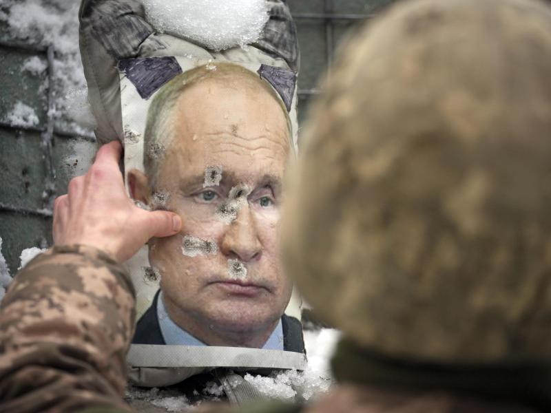 Ein ukrainischer Soldat justiert ein von Kugeln durchlöchertes Bild des russischen Präsidenten Putin. Foto: Vadim Ghirda/AP/dpa