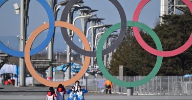Von Olympia-Stimmung ist in Peking wenig zu spüren: Volunteers stehen vor den olympischen Ringen für ein Selfie. Foto: Peter Kneffel/dpa