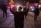 Eine Demonstrantin steht bei einem Protest gegen Polizeigewalt in Oakland mit hochgestreckten Armen vor Polizisten. Foto: Ethan Swope/AP/dpa