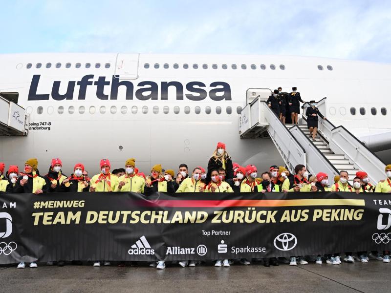 Das deutsche Olympia-Team steht bei der Rückkehr von den Winterspielen auf dem Frankfurter Flughafen hinter einem Plakat: «Team Deutschland zurück aus Peking». Foto: Arne Dedert/dpa