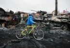 Ein Mann in Butscha schiebt sein Fahrrad an den Überresten eines russischen Militärfahrzeugs vorbei. Foto: Serhii Nuzhnenko/AP/dpa