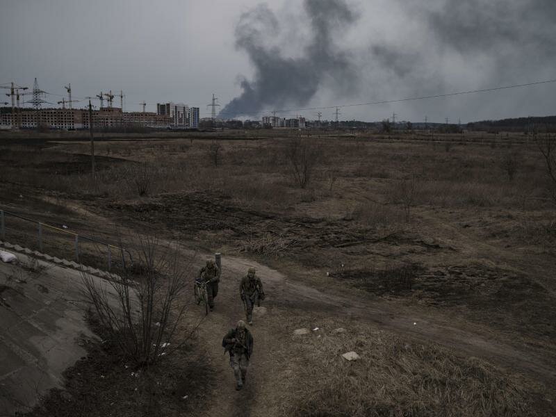 Soldaten gehen einen Weg entlang, während Rauch in Irpin nordwestlich von&nbsp;Kiew aufsteigt. Foto: Felipe Dana/AP/dpa