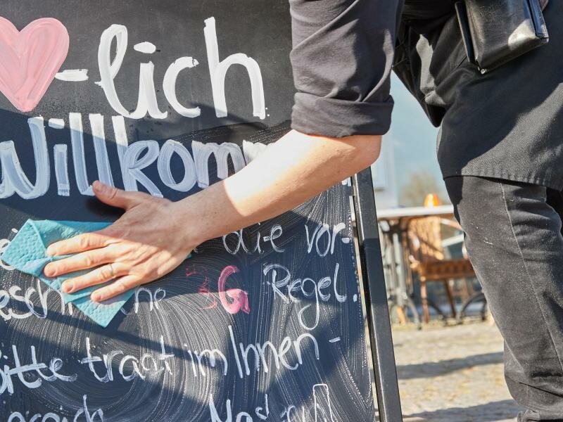 Kellner Tonet Devolli vom Restaurant Mühlstein in Wedel beseitigt die Hinweise zu den 3G-Regeln. Foto: Georg Wendt/dpa