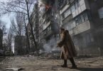Eine Frau in Mariupol geht an einem brennenden Wohnhaus vorbei. Foto: Evgeniy Maloletka/AP/dpa