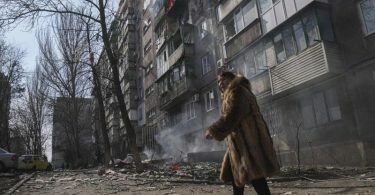 Eine Frau in Mariupol geht an einem brennenden Wohnhaus vorbei. Foto: Evgeniy Maloletka/AP/dpa