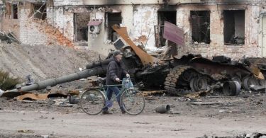 Ein Anwohner geht mit seinem Fahrrad in Trostjanez rund 400 km östlich von Kiew vor beschädigten Gebäuden und einem zerstörten Panzer entlang. Foto: Efrem Lukatsky/AP/dpa