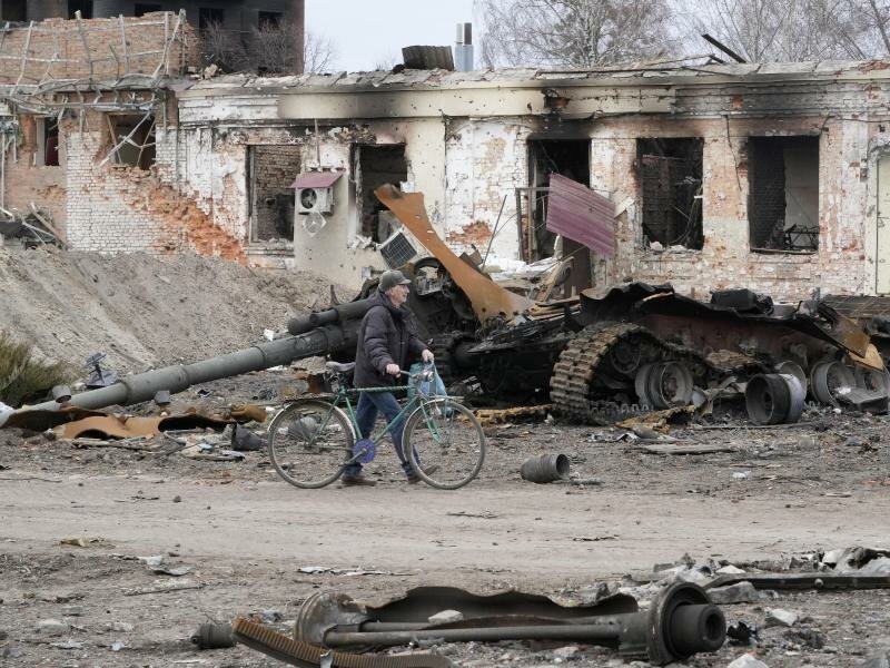 Ein Anwohner geht mit seinem Fahrrad in Trostjanez rund 400 km östlich von Kiew vor beschädigten Gebäuden und einem zerstörten Panzer entlang. Foto: Efrem Lukatsky/AP/dpa