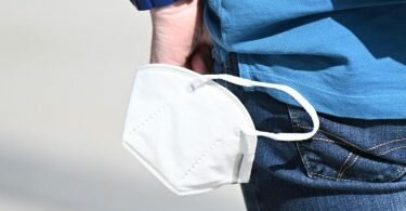 Ein Mann trägt an seinem Handgelenk eine Schutzmaske. Foto: Bernd Weißbrod/dpa