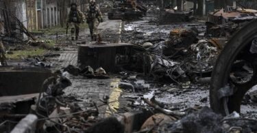 Zwei ukrainische Soldaten inspizieren in Butscha eine mit zerstörten russischen Militärfahrzeugen übersäte Straße. Foto: Rodrigo Abd/AP/dpa