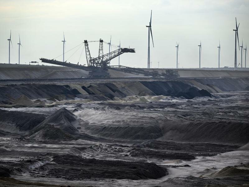 Bergbaumaschinen arbeiten im Braunkohletagebau Garzweiler, im Hintergrund Windräder. Foto: Federico Gambarini/dpa