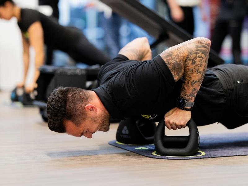 Mitarbeiter Zack führt an einem Messestand auf der Fitnessmesse Fibo ein Muskeltraining aus. Foto: Rolf Vennenbernd/dpa