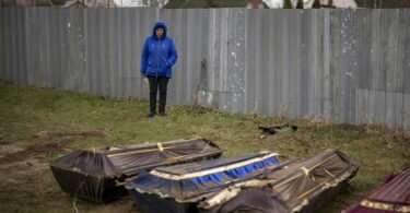 Eine Frau steht während der Exhumierung eines Massengrabes neben Särgen in Butscha. Foto: Emilio Morenatti/AP/dpa