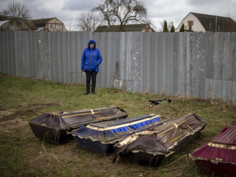 Eine Frau steht während der Exhumierung eines Massengrabes neben Särgen in Butscha. Foto: Emilio Morenatti/AP/dpa