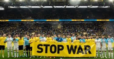 Vor dem Spiel geben beide Teams mit einem Banner ein Statement gegen den Krieg in der Ukraine ab. Foto: Bernd Thissen/dpa
