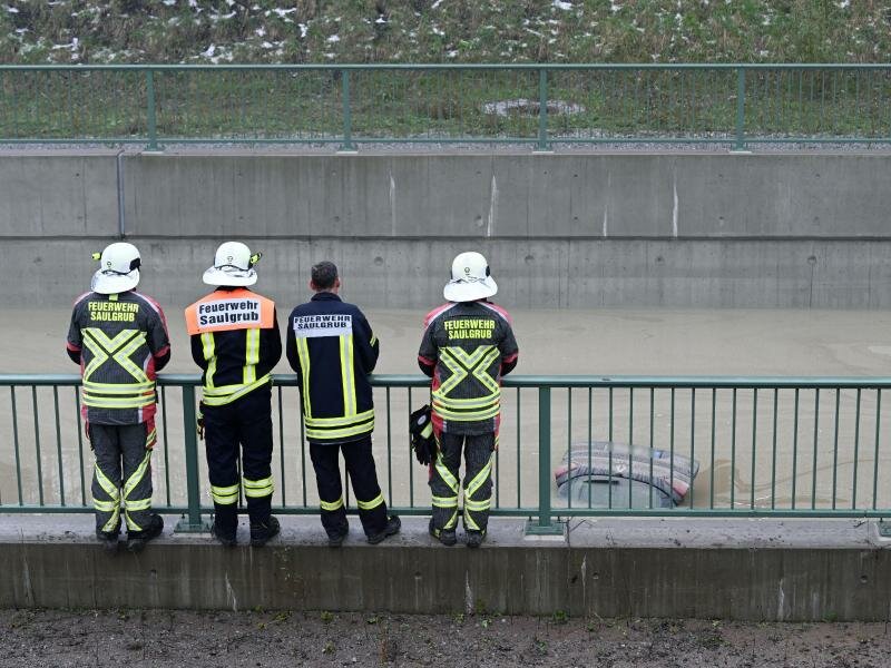 Einsatzkräfte der Feuerwehr schauen auf die Heckklappe eines Autos, das aus dem Wasser auf der teilweise überfluteten Bundesstraße B23 ragt. Foto: Angelika Warmuth/dpa