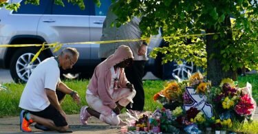 Menschen knien vor Blumen, um den Opfern tödlicher Schüsse in einem Supermarkt in Buffalo die letzte Ehre zu erweisen. Foto: Matt Rourke/AP/dpa