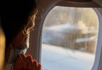 Ein weiblicher Fluggast mit Maske schaut vor dem Start aus dem Fenster. Auf Flügen von und nach Deutschland muss weiter Maske getragen werden. Foto: Andreas Arnold/dpa