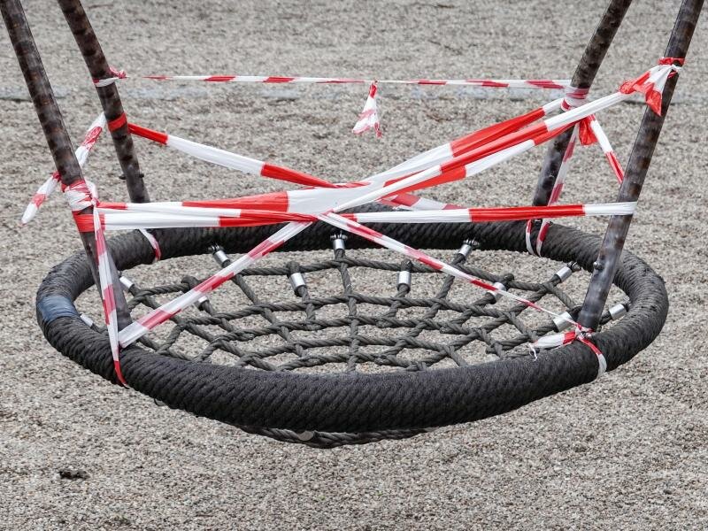 Eine Nestschaukel auf einem gesperrten Spielplatz im Leipziger Rosenthal ist mit rot-weißem Flatterband umwickelt. Foto: Jan Woitas/dpa