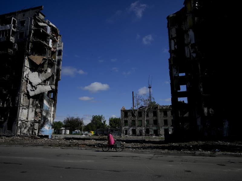 Eine Frau radelt in Borodjanka an zerstörten Wohnhäusern vorbei. Foto: Natacha Pisarenko/AP/dpa