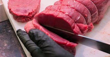 Ein Fleischer zeigt, wie er Steaks von einem Stück Rind quer zur Faser schneidet. Foto: Karolin Krämer/dpa-tmn
