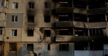 Ein Mann fährt mit dem Fahrrad vor einem zerstörten Gebäude in Borodjanka am Stadtrand von Kiew. Foto: Natacha Pisarenko/AP/dpa