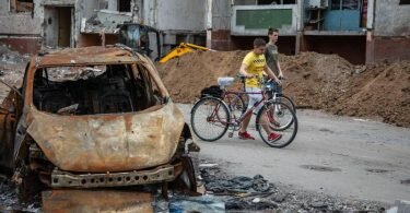 Zwei Jungen schieben ihre Fahrräder an zerstörten Autos und Wohngebäuden in Tschernihiw vorbei. Foto: Michal Burza/ZUMA Press Wire/dpa